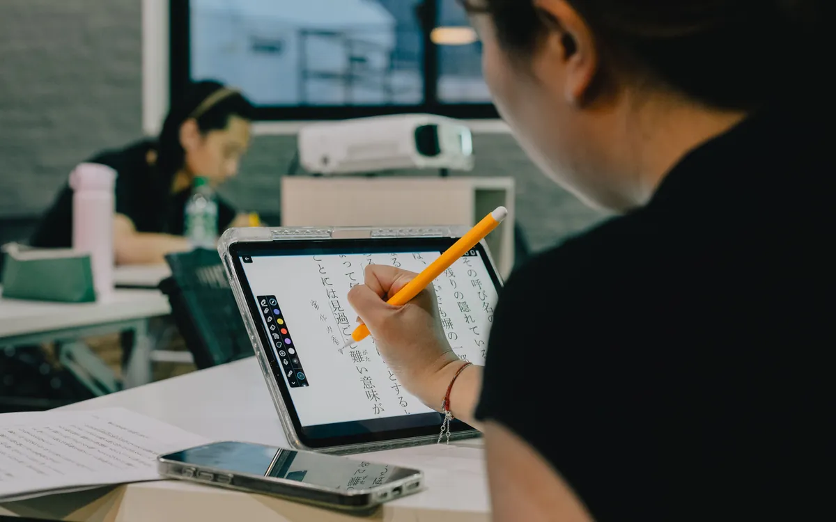 A student writing with a stylus on a modern tablet in a classroom