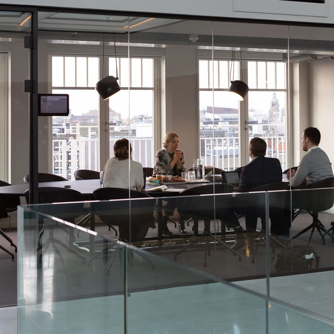 A team meeting in a glass-walled boardroom with tall windows over the city